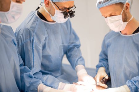 Photo for Three confident surgeons performing surgical operation on a patients knee in operating room. Concept of real surgery and invasive treatments - Royalty Free Image