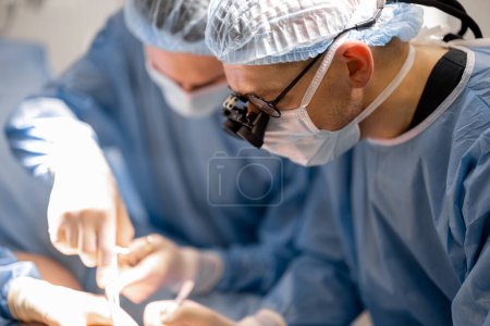 Photo for Three confident surgeons performing surgical operation on a patients knee in operating room. Concept of real surgery and invasive treatments - Royalty Free Image