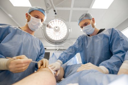 Photo for Confident surgeons performing surgical operation on a patients knee in operating room. Concept of real surgery and invasive treatments - Royalty Free Image