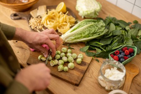 Photo for Man cutting brussels sprouts on cutting board cooking vegetarian pasta, close-up - Royalty Free Image