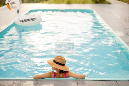 Téléchargez les photos : Femme au chapeau repose à la piscine, vue de derrière - en image libre de droit