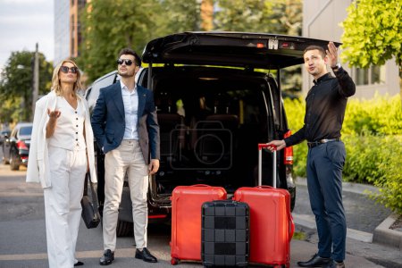Téléchargez les photos : Couple d'affaires debout par un taxi minibus attendant leur chauffeur ou leur porteur pour les aider avec une valise. Concept de voyages d'affaires et de voyages - en image libre de droit