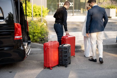 Téléchargez les photos : Chauffeur ou concierge aide un couple d'affaires à transporter leurs valises au bureau ou à l'hôtel à partir d'un taxi minibus. Concept de voyage d'affaires et de service de transport - en image libre de droit