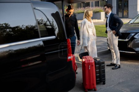 Téléchargez les photos : Couple d'affaires debout par un taxi minibus attendant leur chauffeur ou leur porteur pour les aider avec une valise. Concept de voyages d'affaires et de voyages - en image libre de droit