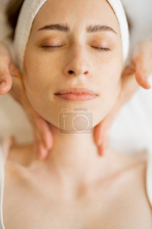 Téléchargez les photos : Femme adulte bénéficiant d'un massage facial relaxant, vue rapprochée d'en haut sur le visage des femmes lors d'un massage. Belle pose de masseurs doigts - en image libre de droit