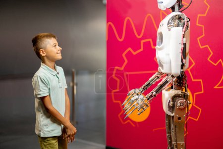 Foto de El niño mira al robot humanoide con una gran emoción, visitando el museo de ciencias. Concepto de nuevas tecnologías y educación infantil - Imagen libre de derechos