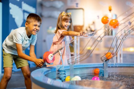 Foto de Niño y niña juegan con pelotas, aprendiendo fenómenos físicos de una manera interesante, divirtiéndose en un museo de ciencias con modelos interactivos - Imagen libre de derechos