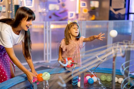 Foto de Mamá con niños juega con pelotas, aprendiendo fenómenos físicos de una manera interesante, divirtiéndose en un museo de ciencias con modelos interactivos - Imagen libre de derechos