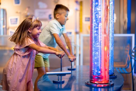 Foto de Niños pequeños bombean burbujas en tubos que estudian fenómenos físicos de una manera interactiva, visitando juntos el museo de ciencias - Imagen libre de derechos