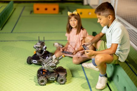 Téléchargez les photos : Enfants jouant avec des voitures robotisées les contrôlant avec des télécommandes sur une aire de jeux dans le musée des sciences. Concept de divertissement pour enfants et nouvelles technologies - en image libre de droit