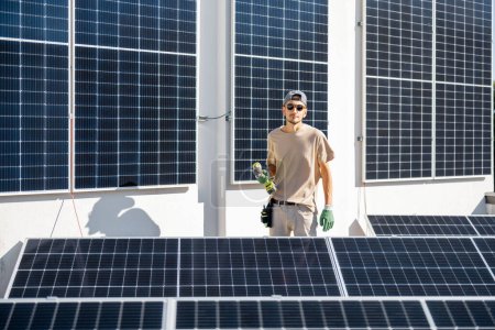 Téléchargez les photos : Portrait d'homme à tout faire debout sur un toit avec des panneaux solaires installés dessus. Concept d'énergies renouvelables pour l'autoconsommation - en image libre de droit