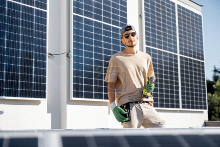 Téléchargez les photos : Portrait d'homme à tout faire debout sur un toit avec des panneaux solaires installés dessus. Le concept des énergies renouvelables pour l'autoconsommation. Idée d'installation de panneaux pour les ménages - en image libre de droit