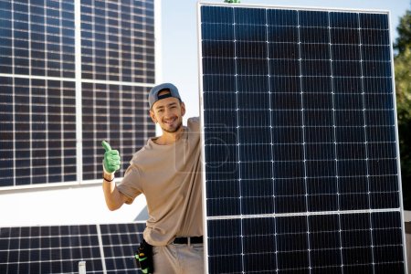 Téléchargez les photos : Portrait d'un homme debout avec un panneau solaire sur un toit de sa maison pendant le processus d'installation. Propriétaire de la propriété installant des panneaux solaires pour l'autoconsommation - en image libre de droit