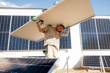Foto de El hombre lleva el panel solar sobre sus hombros mientras instala la planta solar de una azotea de su propiedad. Energía renovable para autoconsumo. Idea de instalar paneles para los hogares - Imagen libre de derechos