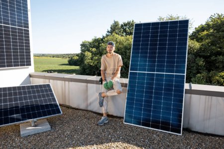 Téléchargez les photos : Portrait d'un homme assis sur le toit de sa maison pendant le processus d'installation d'une centrale solaire. Concept d'énergies renouvelables et de durabilité - en image libre de droit