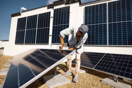 Téléchargez les photos : Homme installant des panneaux solaires sur le toit de sa maison, cellule à visser sur le toit plat pour l'autoconsommation. Concept d'énergies renouvelables et de durabilité - en image libre de droit