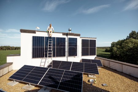 Téléchargez les photos : Toit d'une maison privée avec une centrale solaire dessus, l'homme assis sur un toit et profite de sa propriété. Concept d'énergie renouvelable et mode de vie durable - en image libre de droit
