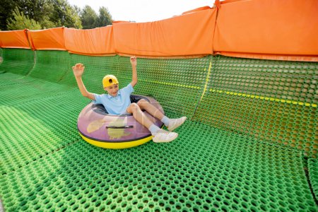 Foto de Niño feliz desciende en tubo de trineo inflable en una pista de verano, divirtiéndose en el parque de atracciones. Concepto de vacaciones de verano y entretenimiento infantil - Imagen libre de derechos
