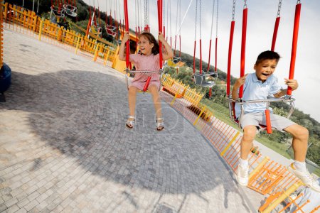 Téléchargez les photos : Enfants chevauchant sur carrousel d'amusement coloré tout en visitant le parc d'attractions pendant des vacances d'été - en image libre de droit