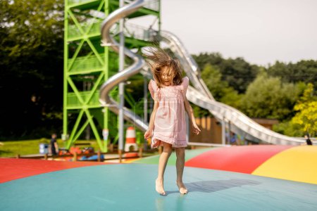 Foto de Niña saltando en trampolín inflable, divirtiéndose visitando el parque de atracciones durante unas vacaciones de verano - Imagen libre de derechos