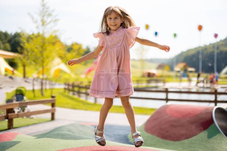 Foto de Niña saltando en trampolín inflable, divirtiéndose visitando el parque de atracciones durante unas vacaciones de verano - Imagen libre de derechos