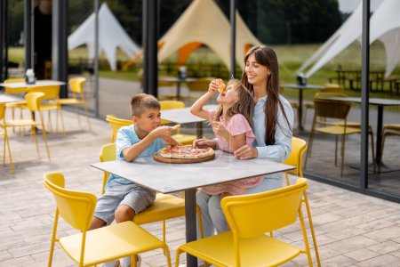 Foto de Mamá con niños comiendo pizza, pasando el verano feliz en el parque de diversiones. Concepto de comida al aire libre, infancia y entretenimiento - Imagen libre de derechos