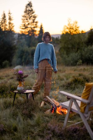 Photo for Woman has a picnic with bonfire while traveling in mountains on sunset - Royalty Free Image