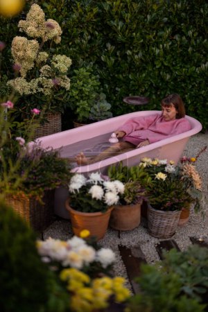 Photo for Cozy backyard with a woman bathing in pink bathtub outdoors at dusk. Concept of relaxation and beauty - Royalty Free Image