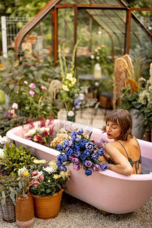 Téléchargez les photos : Femme couchée dans une baignoire rose avec beaucoup de fleurs dans le jardin à l'extérieur. Concept de beauté, thérapie bizarre et fleurie - en image libre de droit