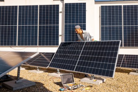 Téléchargez les photos : Homme installant des panneaux solaires sur le toit de sa maison, cellule de montage sur le toit plat pour l'autoconsommation. Concept d'énergies renouvelables et de durabilité - en image libre de droit