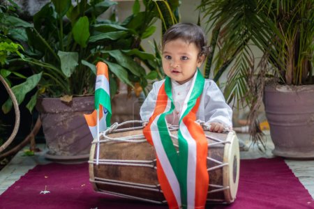 Photo for Cute toddler holding indian tricolor flag with traditional dholak and cloth with innocent face - Royalty Free Image