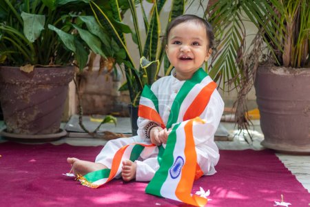 Niedliches Kleinkind mit indischer Trikolore-Flagge in traditionellem Tuch mit unschuldigem Gesichtsausdruck