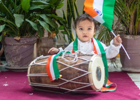 Photo for Cute toddler holding indian tricolor flag with traditional dholak and cloth with innocent face - Royalty Free Image