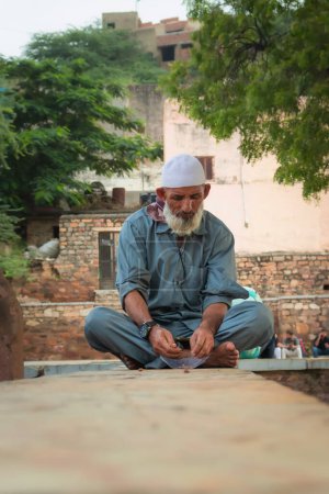 Foto de Anciano indio muselina devoto sentado en la pared de la mezquita en el día desde un ángulo único - Imagen libre de derechos