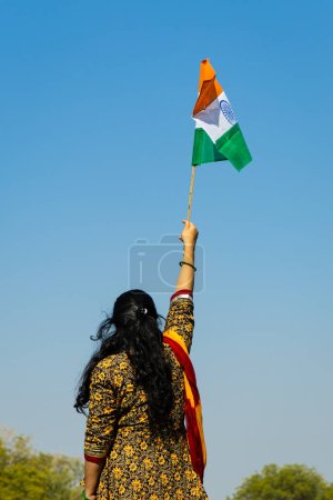 Téléchargez les photos : Jeune fille indienne tenant le drapeau national tricolore indien agitant avec un ciel bleu vif le jour - en image libre de droit