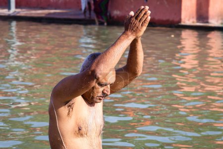 Téléchargez les photos : Dévot prier après la baignade dans l'eau de la rivière sainte le matin sous un angle plat - en image libre de droit