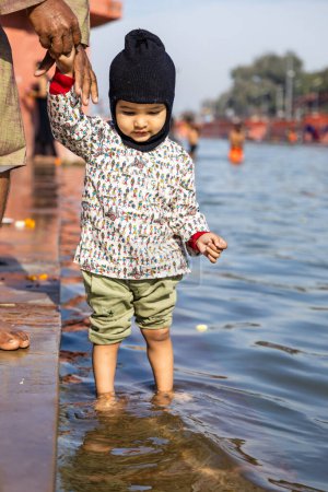 innocent toddler holing grand father finger and standing at holy river at morning from flat angle