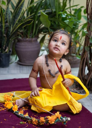 Téléchargez les photos : Portrait de mignon indien garçon robes comme seigneur rama avec arc à l'extérieur avec fond flou le jour - en image libre de droit