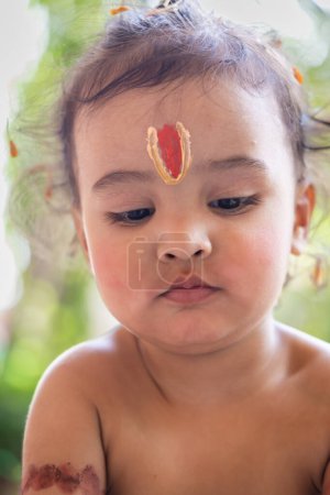 Téléchargez les photos : Mignon garçon indien avec saint symbole religieux sur la tête à l'extérieur avec fond flou - en image libre de droit