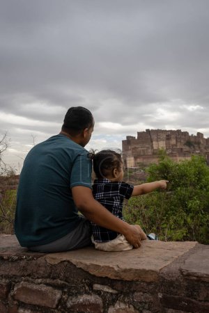 father with infant son watching historical fort at cloudy day image is taken at mehrangarh jodhpur rajasthan india.