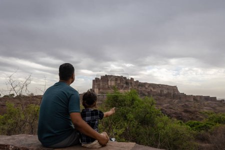 father with infant son watching historical fort at cloudy day image is taken at mehrangarh jodhpur rajasthan india.