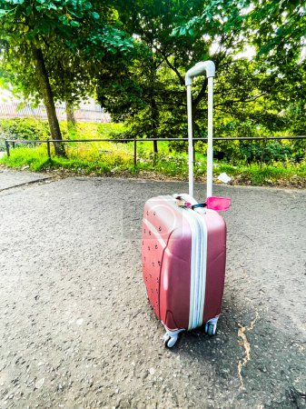 Photo for Pink suitcase with a blank pink tag in a public park in Edimburgh - Royalty Free Image