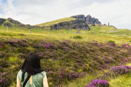 Téléchargez les photos : Plan arrière d'une jeune femme caucasienne aux cheveux bruns observant tranquillement le beau paysage des Highlands écossais, avec le vieil homme de Storr au loin. Espace de copie. - en image libre de droit