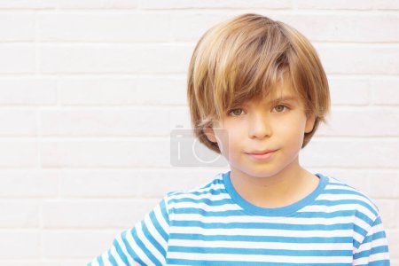 Frontalporträt eines 9-jährigen blondhaarigen, grünäugigen Jungen, der mit neutralem Ausdruck in die Kamera blickt. Vereinzelt auf weißem Hintergrund. Horizontal.