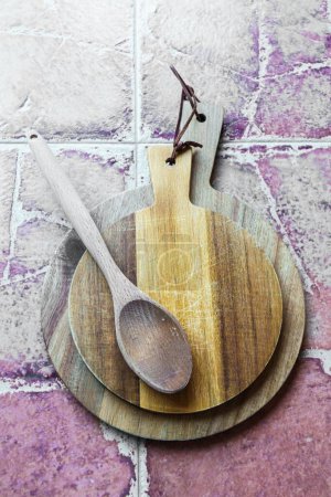 Foto de Vaciar tablas de cortar rústicas de madera junto a una cuchara de madera en un piso de cerámica. Vertical. - Imagen libre de derechos