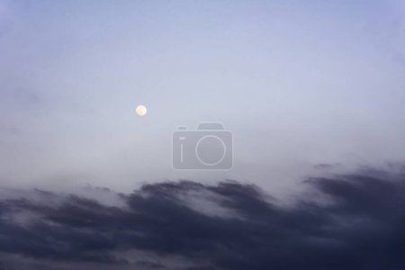 Full moon peeking through the clouds. Bluish sky at dusk. Backgrounds. Copy space.