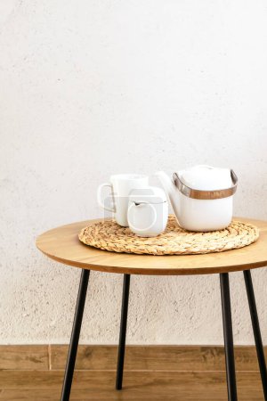 Wooden table with ceramic tea or coffee pottery set against white wall. Vertical. Copy space.
