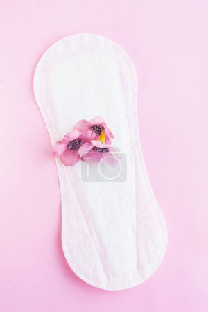 Three pink flowers placed on a white panty liner, metaphor of menstrual blood. Isolated on pink background. Concept of feminine hygiene, sanitary napkins and menstruation. Vertical studio shot.