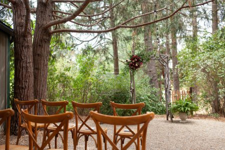 Photo for Vintage wooden arch wtih red and pink roses - outdoor wedding ceremony location in coniferous forest wtih classic bentwood chairs - Royalty Free Image