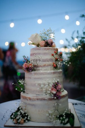 Téléchargez les photos : Beau gâteau de mariage à trois niveaux avec décoration florale rustique. Événement nocturne extérieur. - en image libre de droit